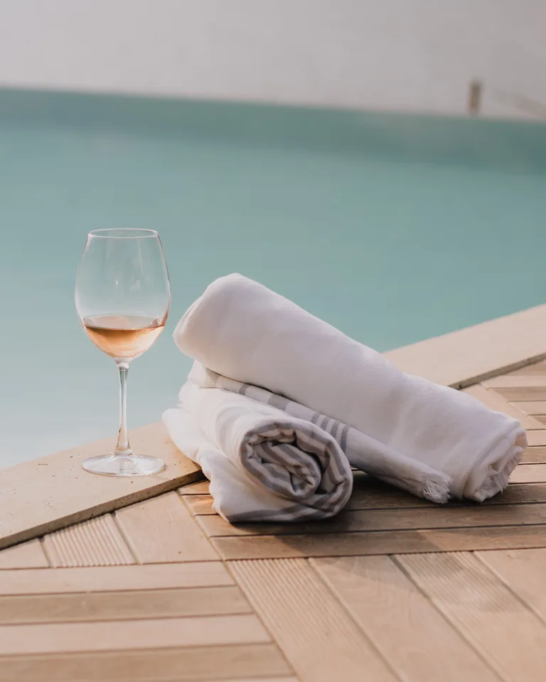 White towels and a glass of wine on a wooden poolside deck