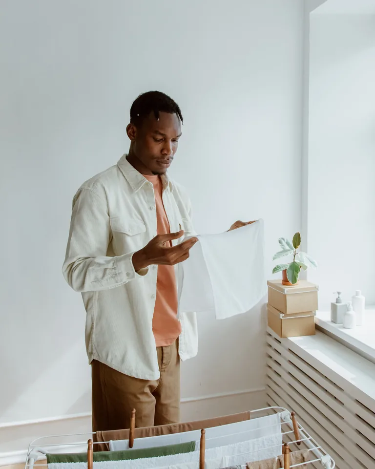 Man hanging fresh laundry on a freestanding rack in a bright room