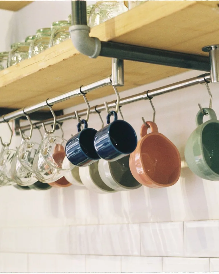 Mugs hanging from hooks under a kitchen shelf