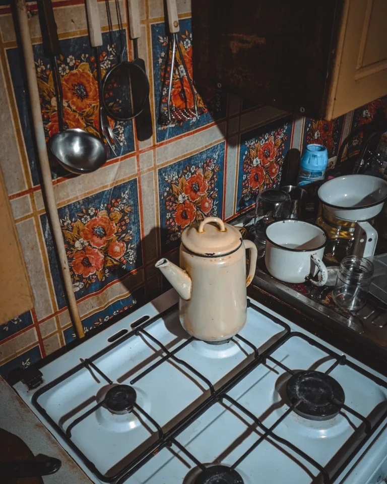 Enamel kettle on a gas stove surrounded by floral wallpaper and utensils