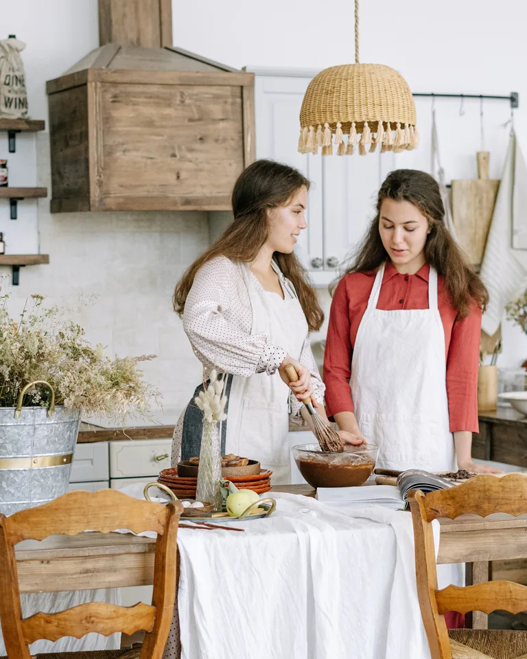 Two women in aprons baking together in a cozy rustic kitchen