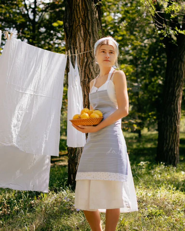 Woman in a garden holding a basket of lemons near a clothesline with white linens