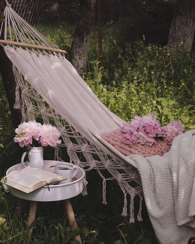 Cozy hammock with pink peonies, a book, and tea on a sunny day