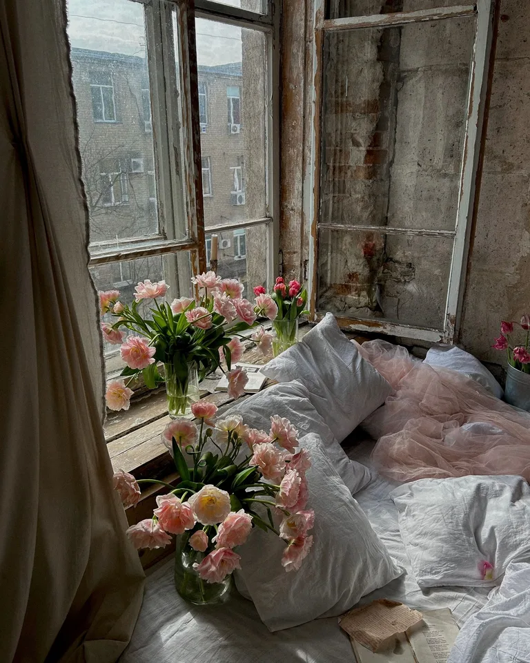 Romantic bed styled with pink roses and soft pillows by an old window