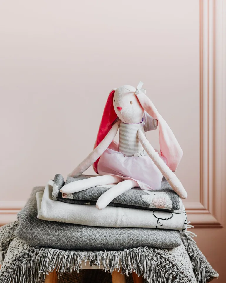 Plush bunny resting on stacked decorative blankets in a cozy setting