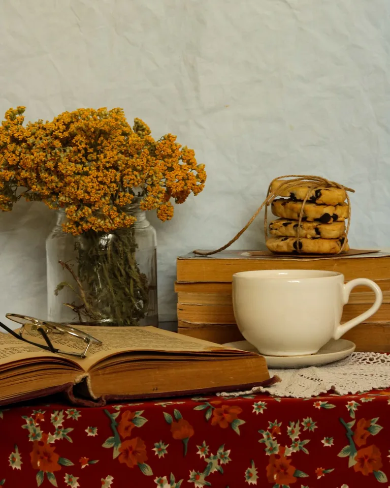 Still life with books, teacup, and flowers on a floral tablecloth