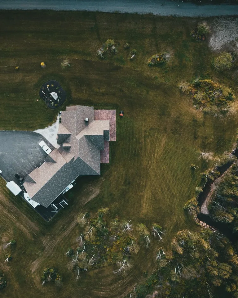 Aerial shot of a suburban house surrounded by lush greenery and a driveway