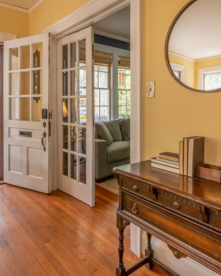 Sunlit entryway with a wooden dresser, mirror, and vase