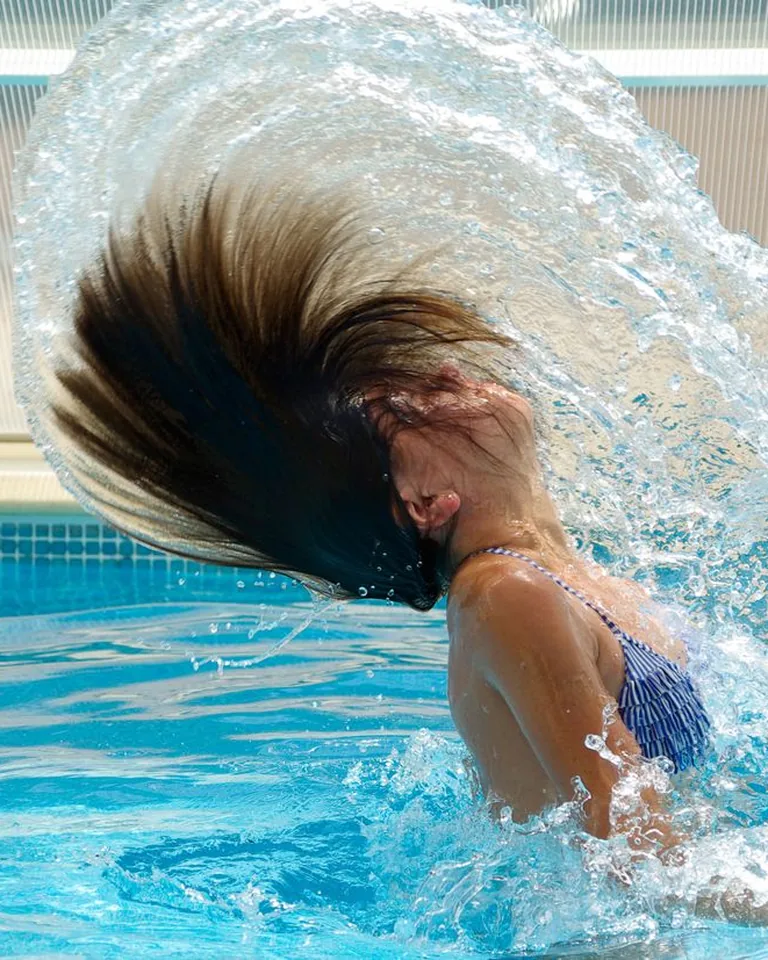 Woman splashing water in a clear blue swimming pool