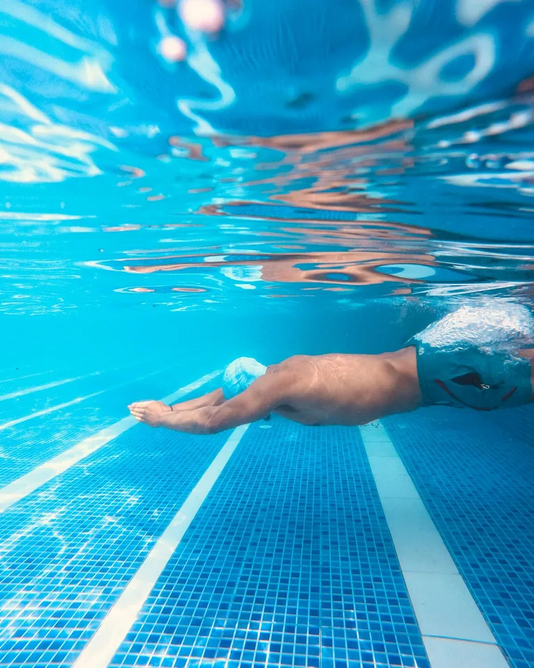 Man swimming underwater in a clear blue pool