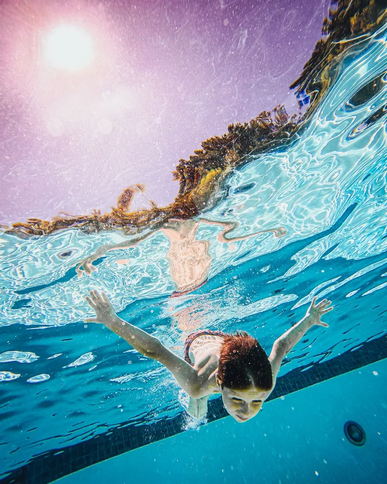 Child swimming underwater in a sunlit pool