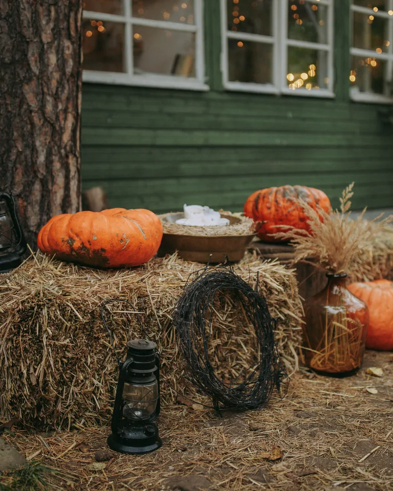 Cozy fall setting with pumpkins, hay bales and lanterns by a wooden house
