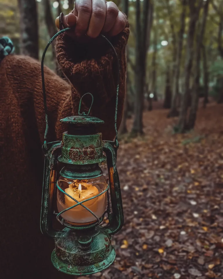 Hand holding a lit lantern in a misty autumn setting