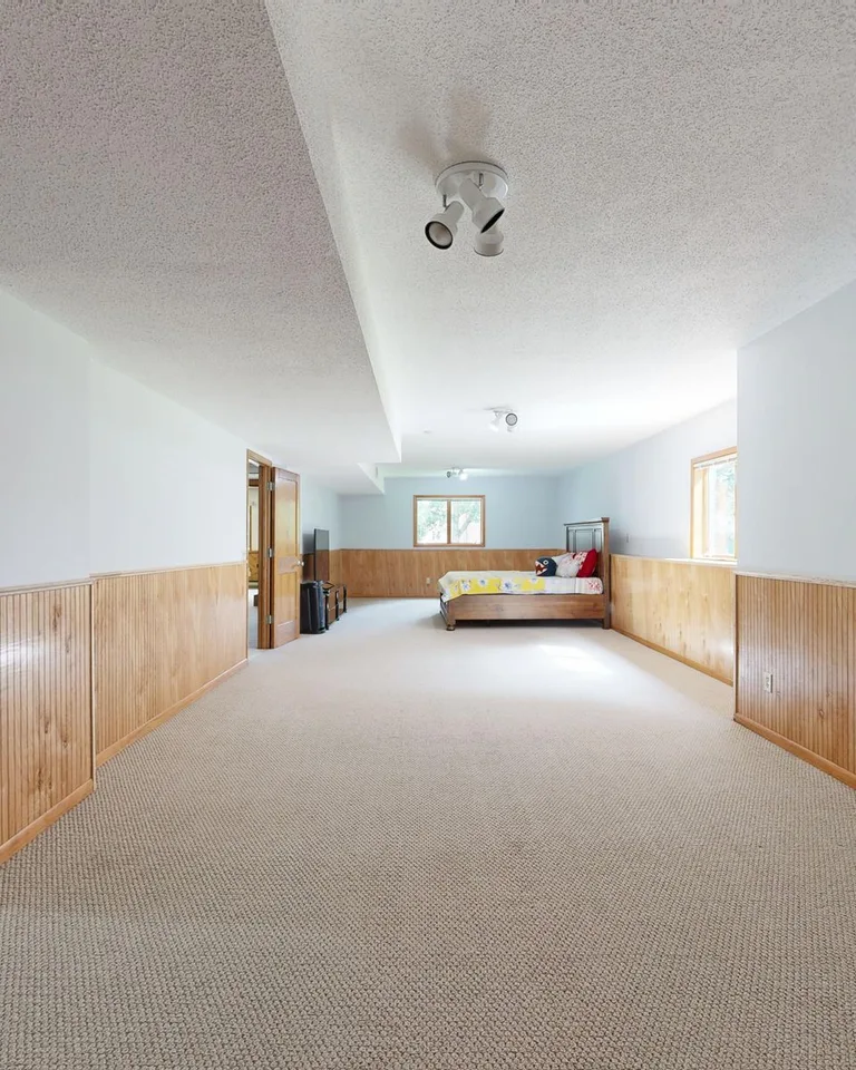 Empty basement room with wooden paneling and carpet flooring