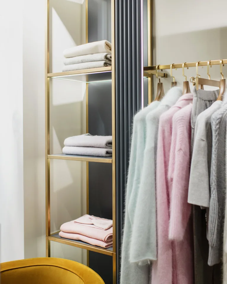 Folded towels on a white wooden shelf beside hanging clothes
