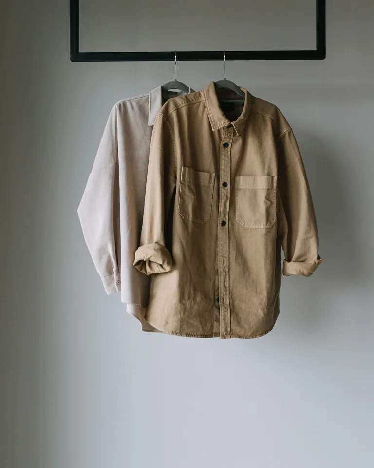 Two neutral shirts hanging on a clothing rack