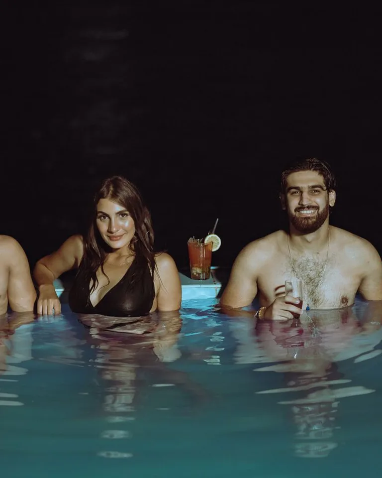 Group of adults smiling and holding drinks in a swimming pool at night