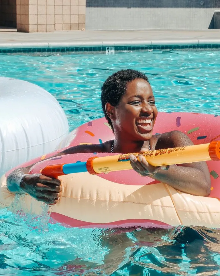 Smiling woman with a swim ring and water gun having fun in a pool