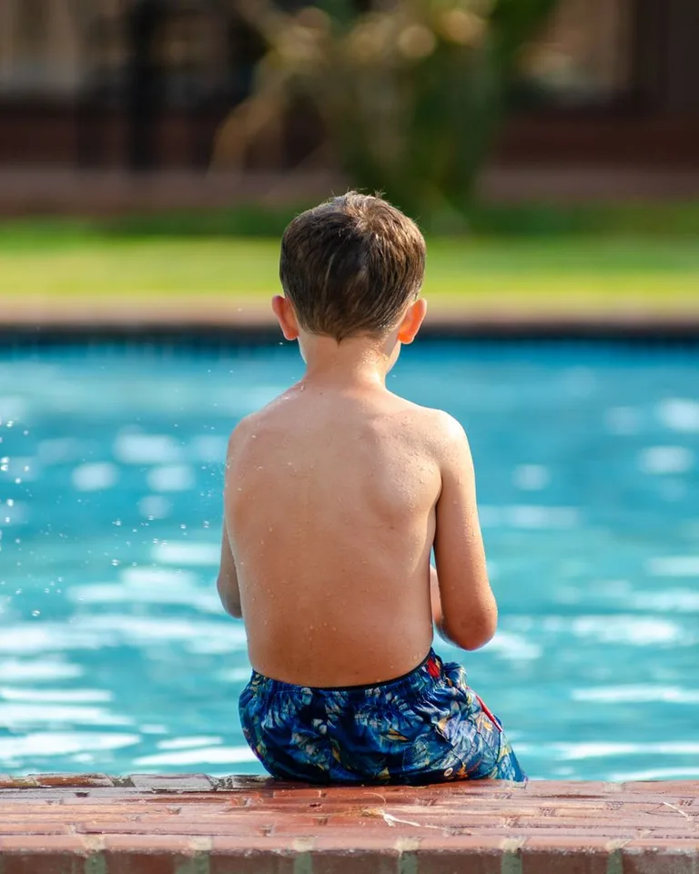 Child sitting on the poolside enjoying a sunny day outdoors