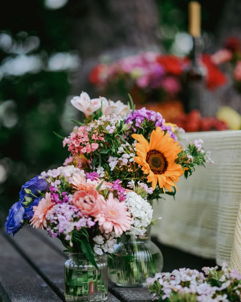 Colorful bouquet of summer flowers in a glass jar on a wooden table outdoors