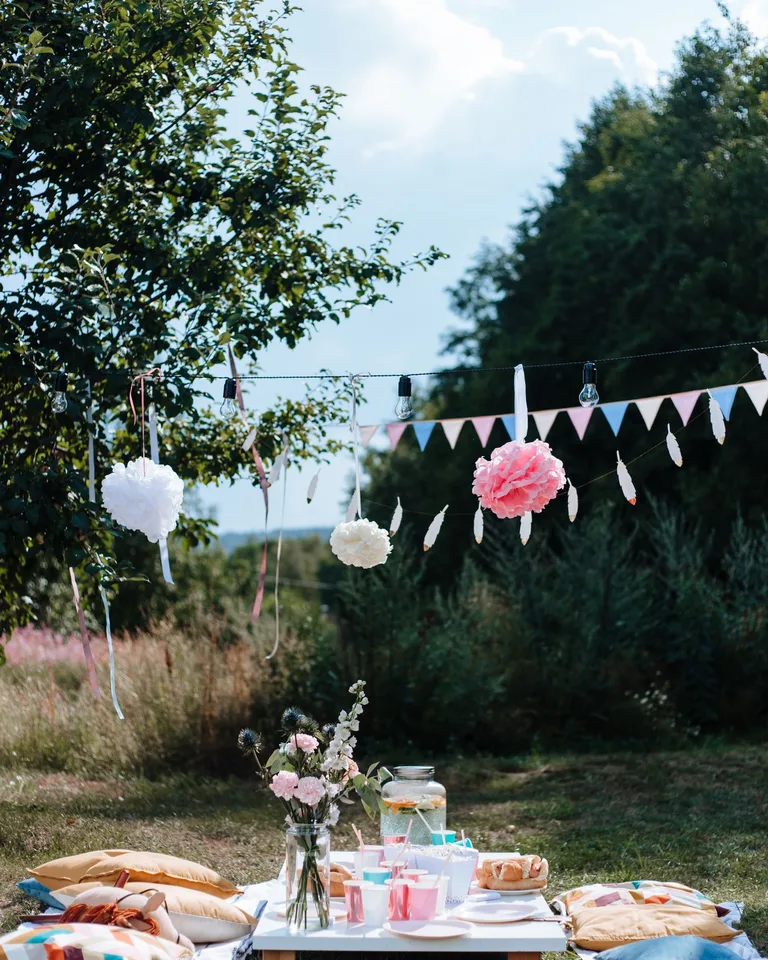 Outdoor picnic setup with vibrant decor, bunting and cushions under a sunny sky