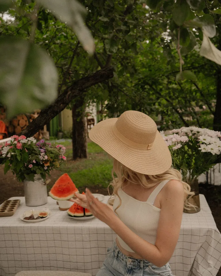 Woman in a summer hat enjoying watermelon outdoors in a serene garden