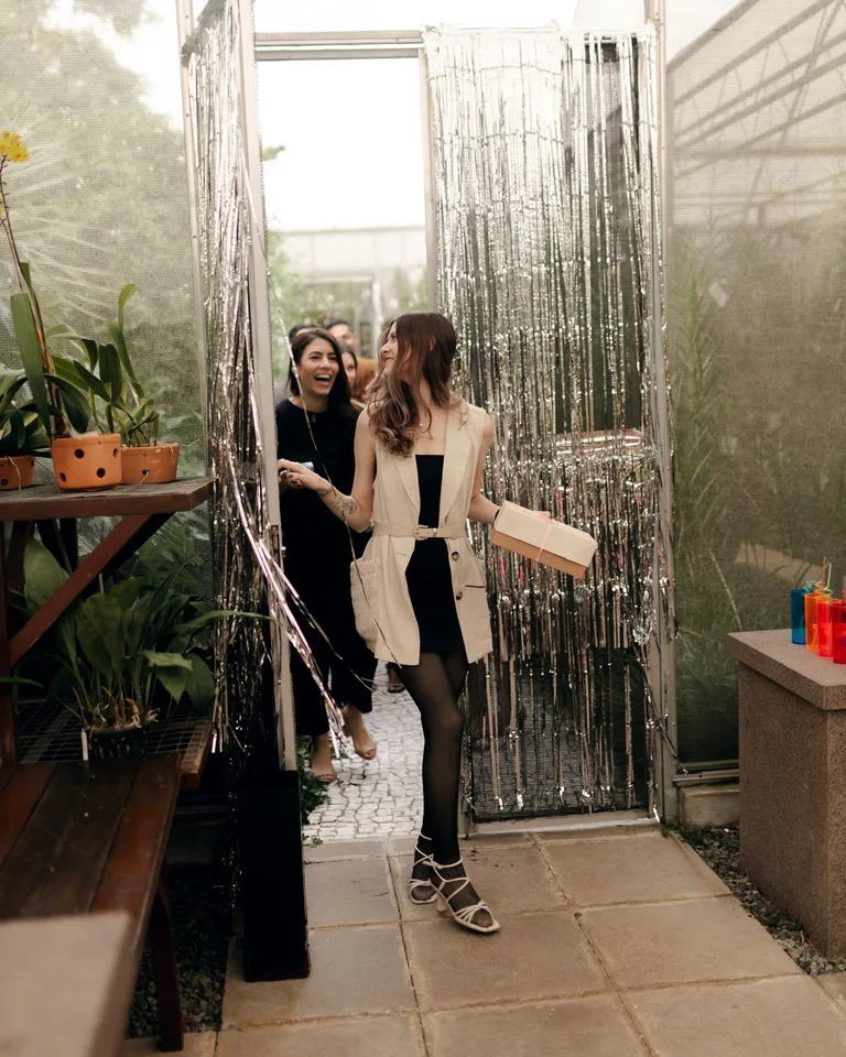 Woman walking through a tinsel door into an outdoor party holding a gift