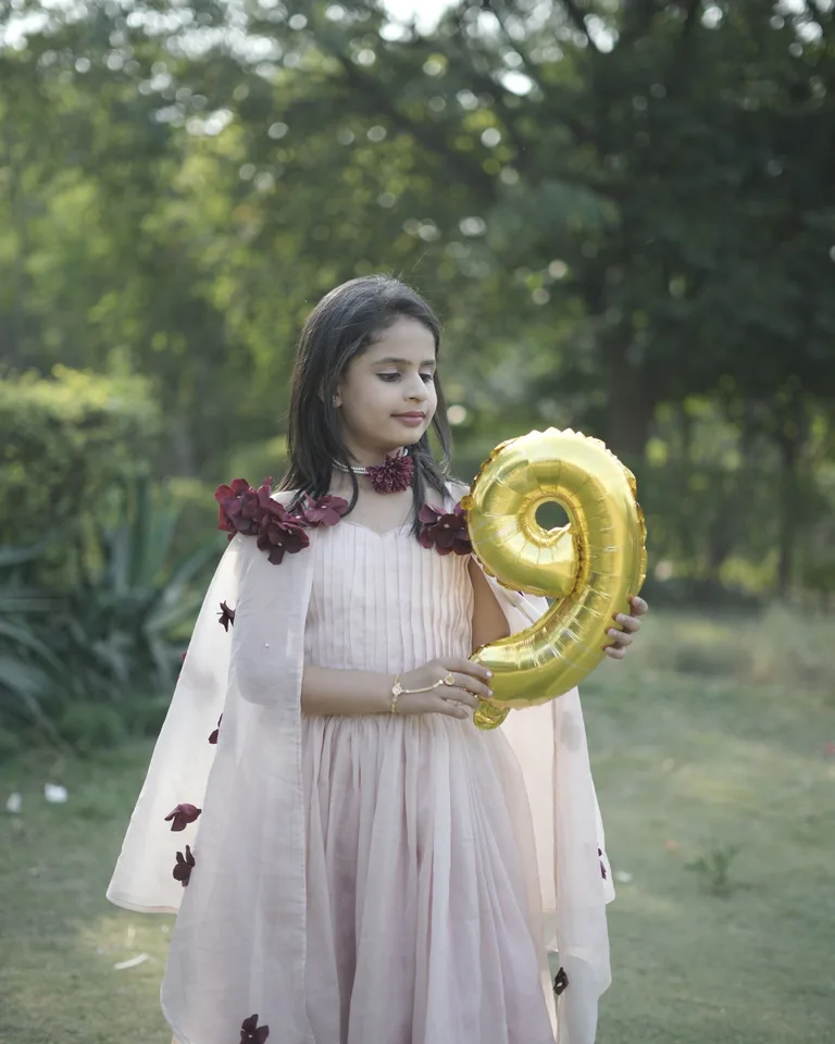 Girl in a pink dress holding a gold number balloon outdoors