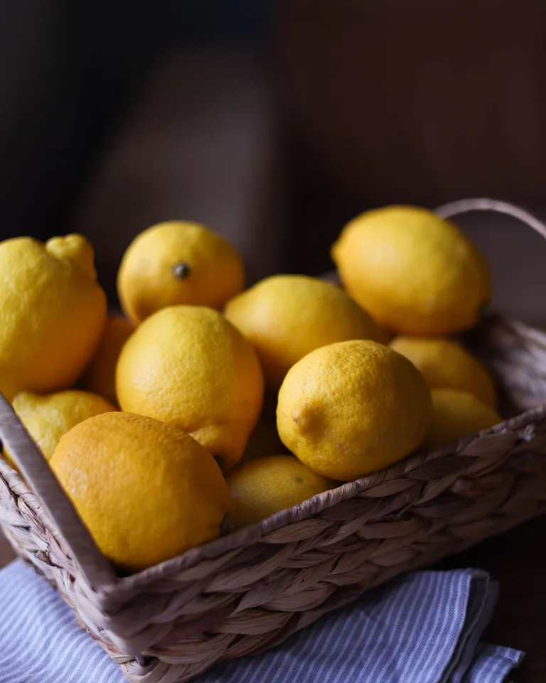 Close-up of bright yellow lemons in a wicker basket on a wooden table